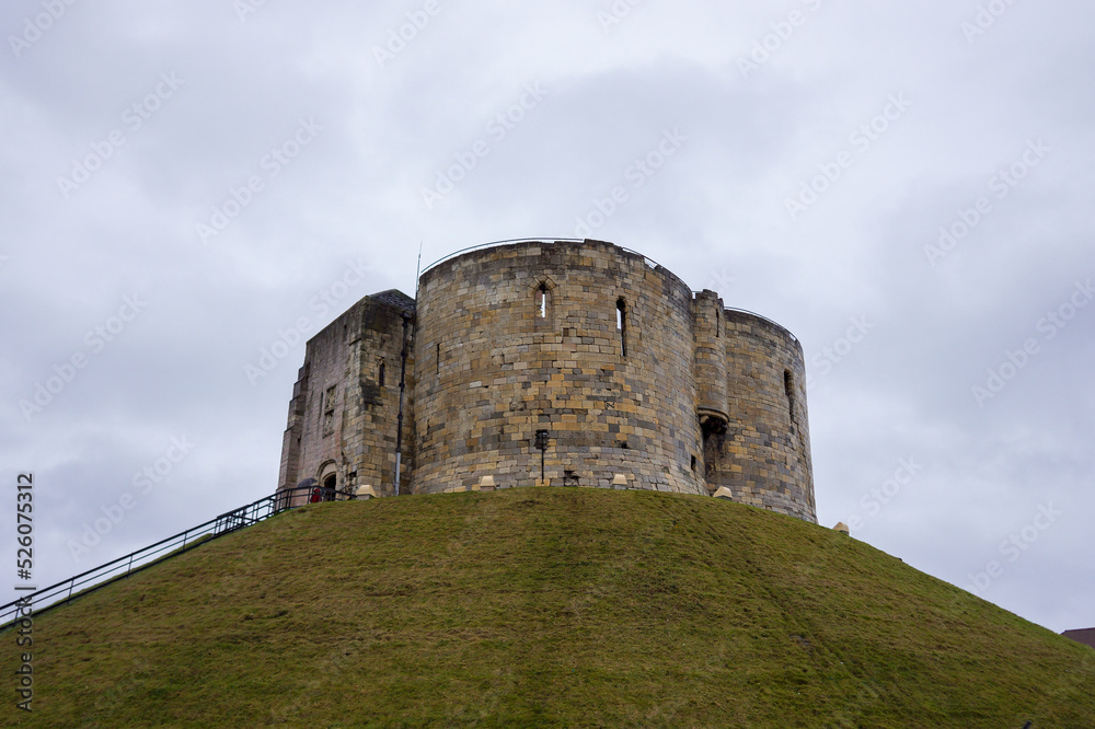View of Clifford's Tower in York, UK with green grass hill and cloudy sky background. No people.