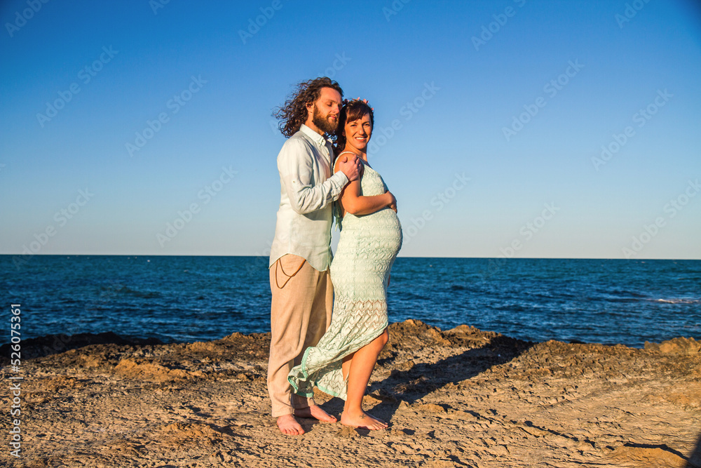 A pregnant couple on a beach during sunset
