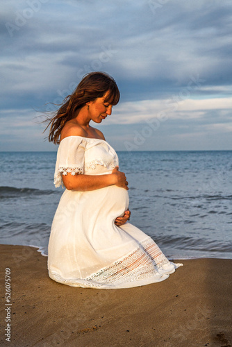 A young pregnant woman on a beach touching her pregnancy belly