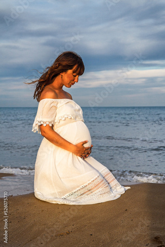 A young pregnant woman on a beach touching her pregnancy belly