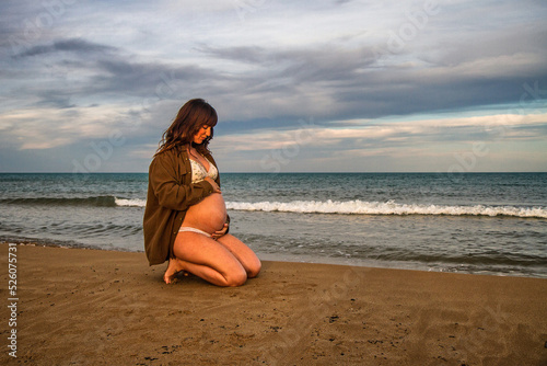 A young pregnant woman on a beach touching her pregnancy belly