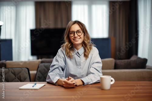Fotografie Smiling female employee wearing glasses sitting at office desk looking at camera