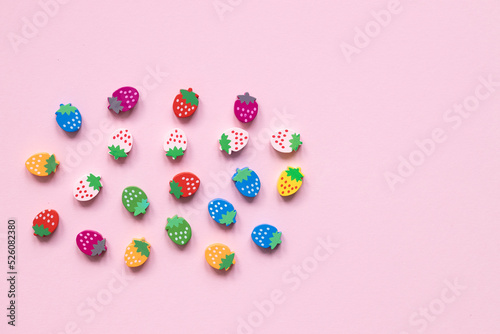 Colored wooden figures in the form of strawberries on a pink background