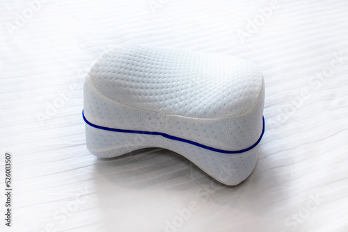 Orthopedic knee pillow for comfortable sleep. The pillow lies on the bed.