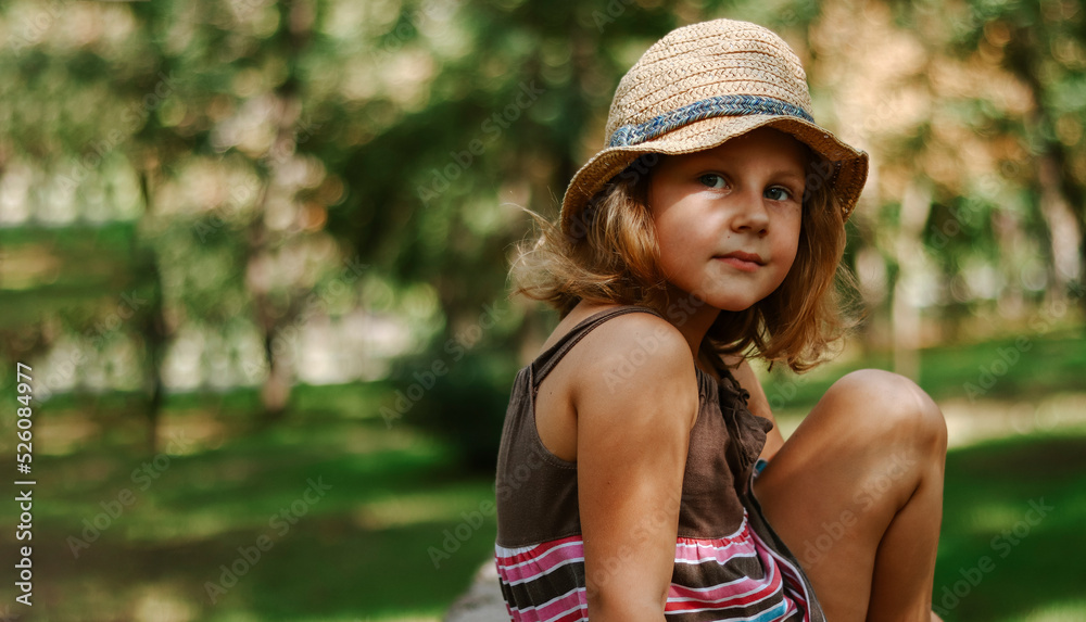 Girl in a straw hat outdoors. Portrait of a cute girl 5 years old. The child is sitting in the park. Copy space.