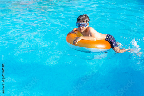 White Eastern European boy 9 years old wearing goggles on a swim ring in the pool. Side view