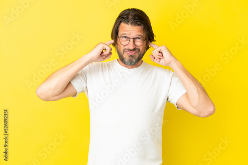 Senior dutch man isolated on yellow background frustrated and covering ears