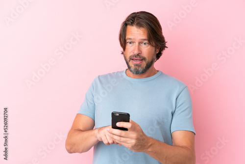Senior dutch man isolated on pink background sending a message or email with the mobile © luismolinero