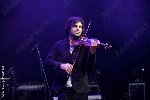 Musician violinist with a violin in his hands standing on stage during the concert. Around the bright light from the floodlights.