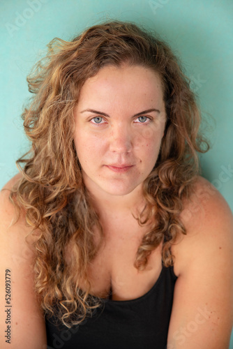 Portrait of a beautiful Caucasian woman with blonde curly hair and blue eyes, looking at the camera with a neutral smile, young good-looking model posing in a studio against a light green background