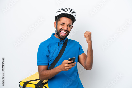 Young Brazilian man with thermal backpack isolated on white background with phone in victory position
