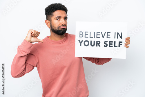 Young Brazilian man isolated on white background holding a placard with text Believe In Your Self with proud gesture