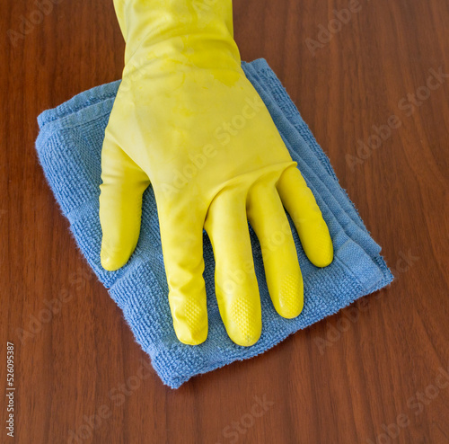 Fotografie, Obraz Latex gloved hand cleaning wood surface with blue cloth towel