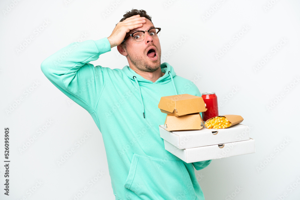 Young caucasian man holding fast food isolated on white background doing surprise gesture while looking to the side Young caucasian man holding fast food isolated on white background doing surprise gesture while looking to the side