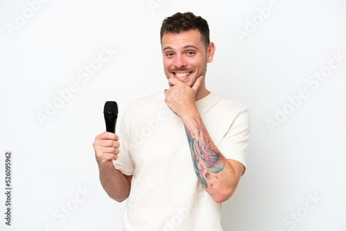 Young caucasian singer man picking up a microphone isolated on white background happy and smiling