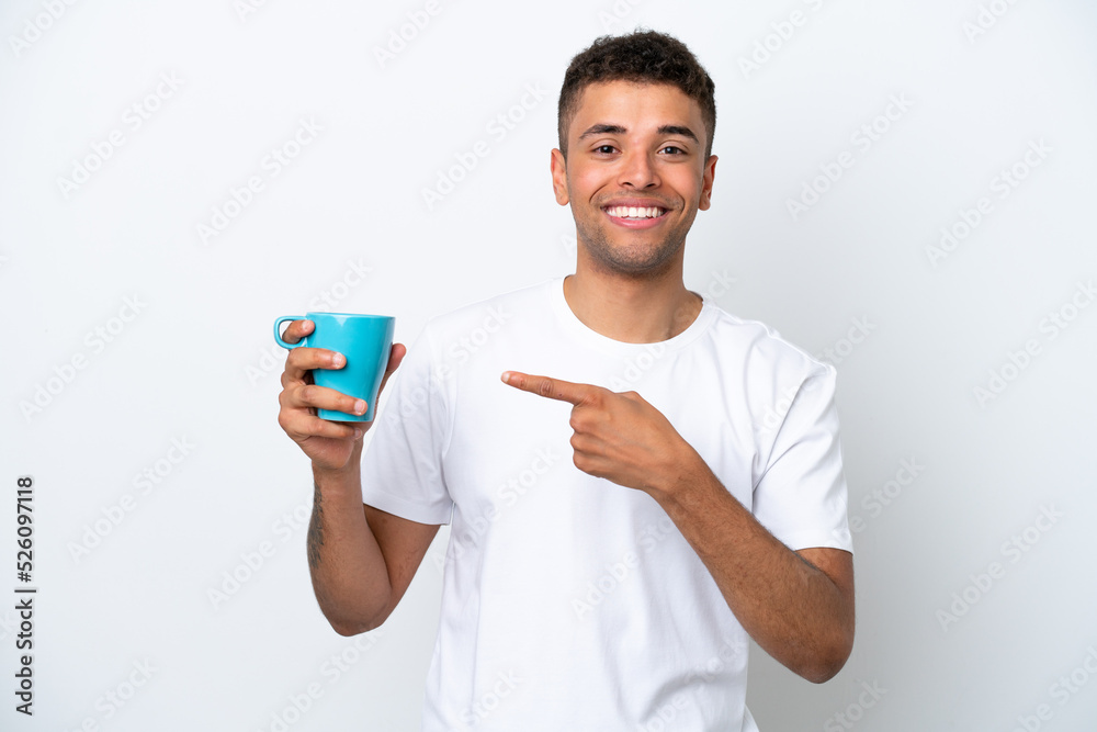 Young Brazilian man holding cup of coffee isolated on white background and pointing it Young Brazilian man holding cup of coffee isolated on white background and pointing it