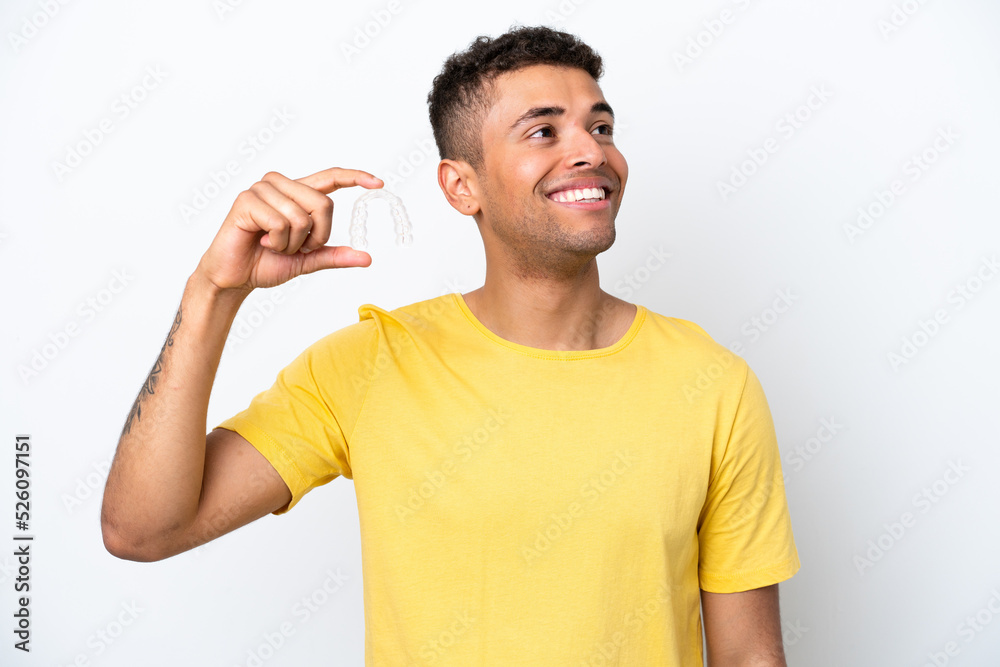 Young Brazilian man holding invisible braces isolated on white background looking up while smiling Young Brazilian man holding invisible braces isolated on white background looking up while smiling