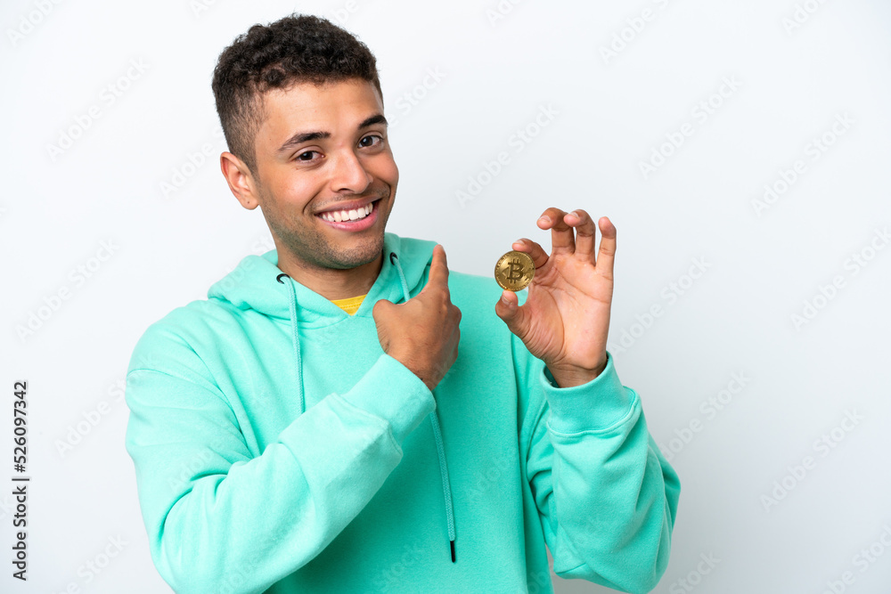Young Brazilian man holding a Bitcoin isolated on white background pointing back