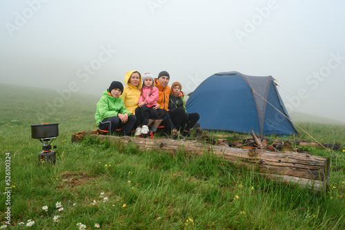 A family in bright clothes sits near a tent in the mountains, morning fog in the mountains.
