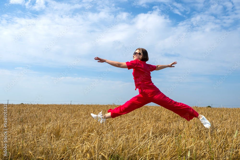 Woman is hovering over wheat. Jumping girl above spikelets with grain. Happy business woman over wheat field. Girl in red suit rejoices in good harvest of wheat. Agricultural business owner Woman is hovering over wheat. Jumping girl above spikelets with grain. Happy business woman over wheat field. Girl in red suit rejoices in good harvest of wheat. Agricultural business owner