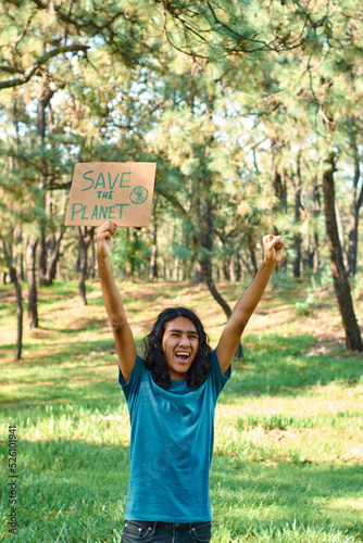 Young teenage man holding sign that says SAVE THE PLANET, in the forest.