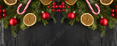 Christmas banner with spruce branches, dried orange and red bead on the black wooden background. Copy space.