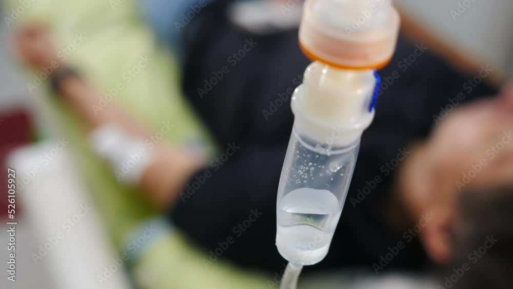 Intravenous drip in focus with blurred patient in background out of focus,infusion dripping. Medical dropper with drug for patients. treatment of diseases. Infusion dripping. Medical IV Drop Rate. 4 k Intravenous drip in focus with blurred patient in background out of focus,infusion dripping. Medical dropper with drug for patients. treatment of diseases. Infusion dripping. Medical IV Drop Rate. 4 k