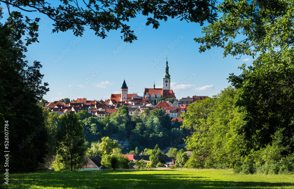 Beautiful look to scenic Tabor old town framed by green tree branches on blue sky. View on gothic church in historical center of medieval hussites city in tranquil summer nature. Czech urban monument.