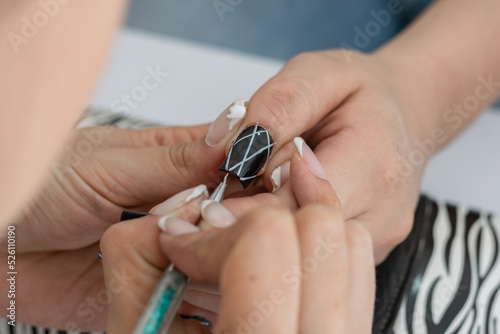detail view of a manicurist's hands learning how to decorate a woman's nails with white lines, outlining with a brush. making a manicure design. concentration to work.