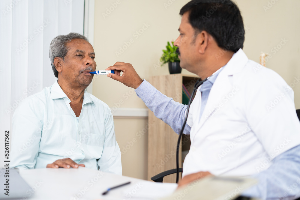 Obraz premium Doctor at clinic checking temperature of sick old man using thermometer due to fever - concept of medical treatment, counselling and health checkup