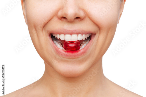 Cropped shot of a young caucasian woman keeping red lozenge for sore throat in her teeth isolated on a white background. Sucking candy in the mouth photo