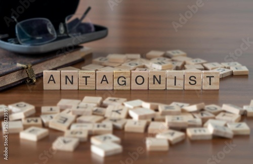 antagonist word or concept represented by wooden letter tiles on a wooden table with glasses and a book photo