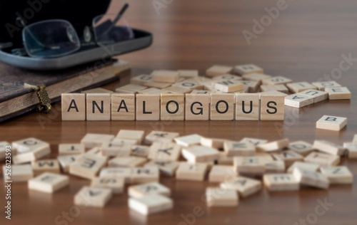 analogous word or concept represented by wooden letter tiles on a wooden table with glasses and a book