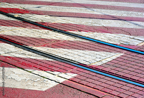 steel streetcar rails in urban setting with pedestrian crossing painted pavement sign. red and white painted cobblestone paving. city transit concept. background image. low angle closeup view.