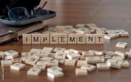 implement word or concept represented by wooden letter tiles on a wooden table with glasses and a book photo