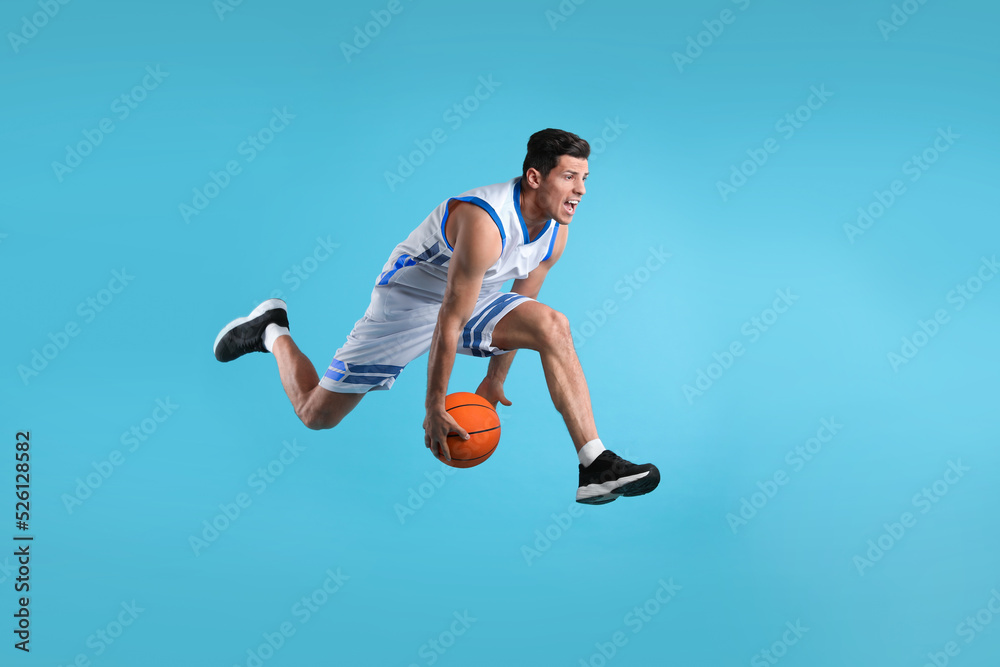 Obraz premium Professional sportsman playing basketball on light blue background