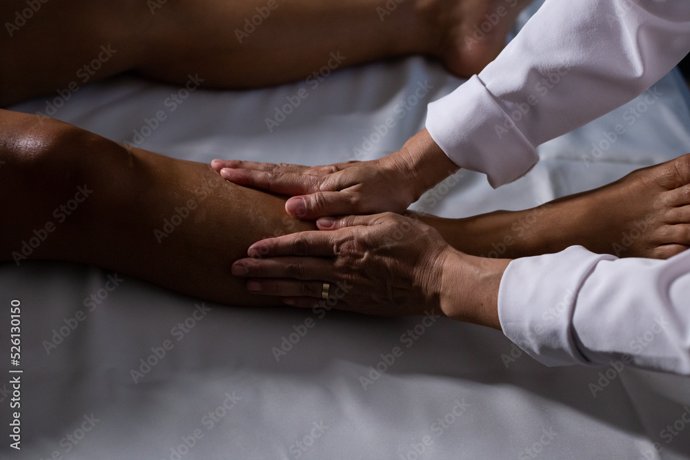 Um profissional fazendo massagem terapeutica nas pernas do paciente que está deitado em uma maca. - obrazy, fototapety, plakaty 