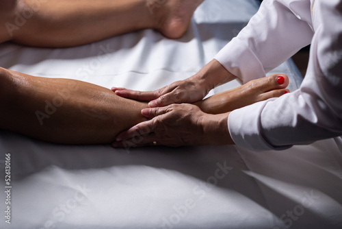 Um profissional fazendo massagem terapeutica nas pernas do paciente que está deitado em uma maca. © Angela