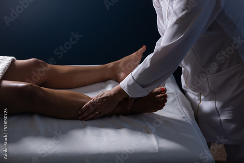 Um profissional fazendo massagem terapeutica nas pernas do paciente que está deitado em uma maca. © Angela
