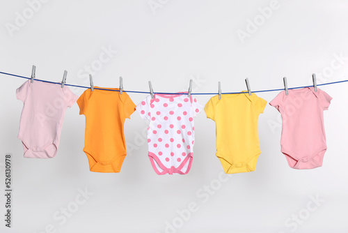 Colorful baby onesies drying on laundry line against light background