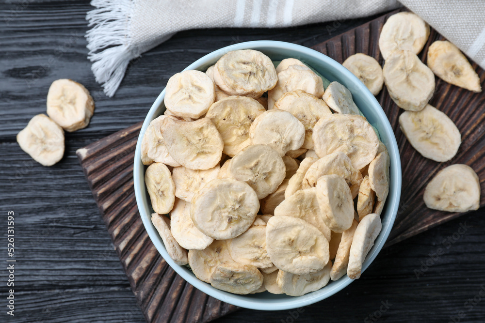 Bowl and dried banana slices on black wooden table, top view Bowl and dried banana slices on black wooden table, top view