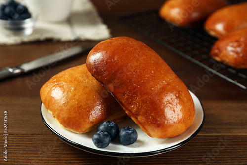 Delicious baked pirozhki with blueberries on wooden table, closeup photo