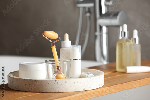 Bath tray with natural face roller and cosmetic products on tub