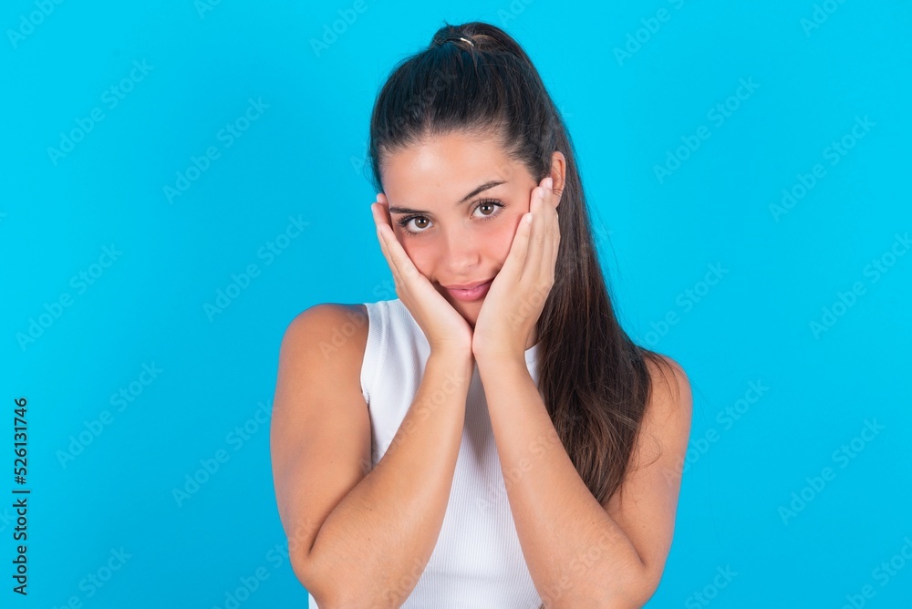Inspired beautiful brunette woman wearing white tank top over blue background looking at copyspace having thoughts about future events Inspired beautiful brunette woman wearing white tank top over blue background looking at copyspace having thoughts about future events