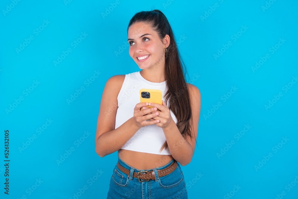 beautiful brunette woman wearing white tank top over blue background holding in hands showing new cell