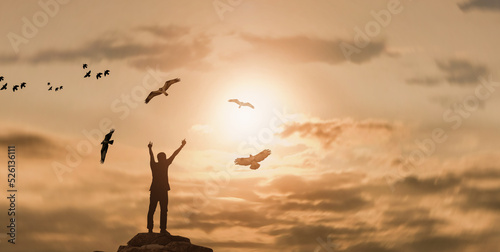 silhouette Man rising hands with eagles flying on the top of a mountain during sunset time. outdoor activity and travel adventure concept © Njay