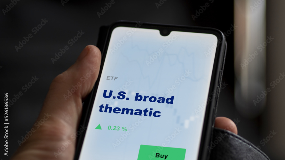 An investor's analyzing the u.s., u.s.a. etf fund on screen. A phone shows the ETF's prices U.S. broad thematic to invest
