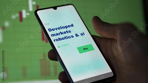 An investor's analyzing the developed markets robotics & ai etf fund on screen. A phone shows the ETF's prices developed market robotics and ai to invest