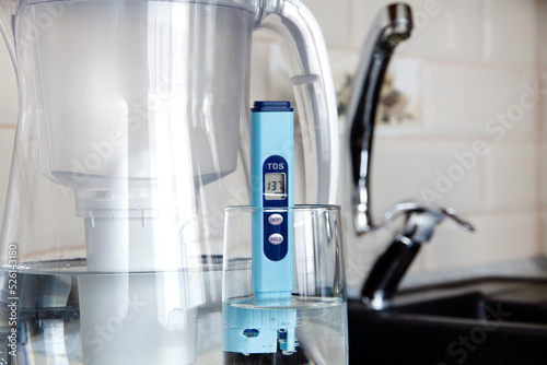  Electronic pH meter in a glass of water. In the background there is a tap for drinking water. The concept of testing water for miralization. Water test