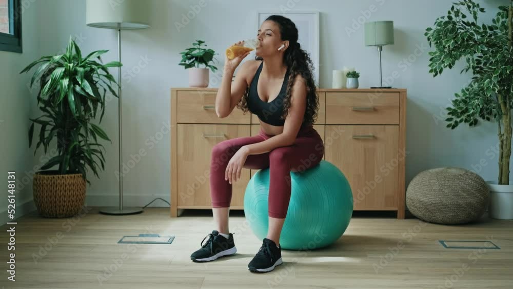 Video of sporty young woman drinking detox juice while doing exercise with the ball at home.